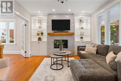 The living room is a true showstopper featuring a sleek gas fireplace with sophisticated porcelain tile surround, custom built-in bookshelves, pot lighting, original hardwood floors, and expansive win - 1371 3Rd Avenue E, Owen Sound, ON - Indoor Photo Showing Living Room With Fireplace