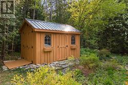 Newer 8x12 garden storage shed with double doors and ramp tucked in the trees. - 