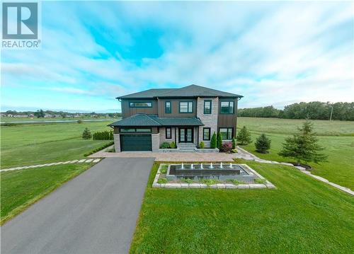 Front of home with lovely landscaping, ornate fountain, long paved driveway & stairs leading to west parking area & to rear of home.   Septic system to left of garage. - 11141 County Road 2 Road, South Dundas, ON - Outdoor