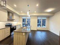 Kitchen with stainless steel range with electric stovetop, a kitchen island with sink, dark wood-type flooring, sink, and wall chimney range hood - 