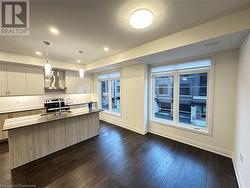 Kitchen with dark wood-type flooring, hanging light fixtures, wall chimney range hood, backsplash, and an island with sink - 