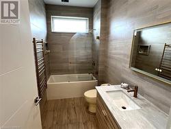 Full bathroom with tile walls, vanity, tiled shower / bath combo, hardwood / wood-style floors, and toilet - 