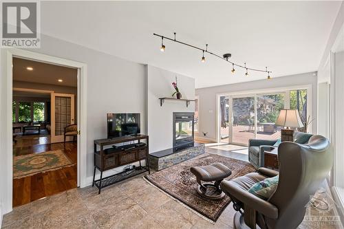 Large sunroom featuring ceramic flooring and 3-way remote controlled fireplace, with walls of windows - 10 Riverbrook Road, Ottawa, ON - Indoor Photo Showing Living Room