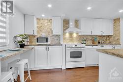 The bright white kitchen offers generous counter and cupboard space, a beautiful backsplash, pot lights, and a breakfast bar, perfect for morning meals - 