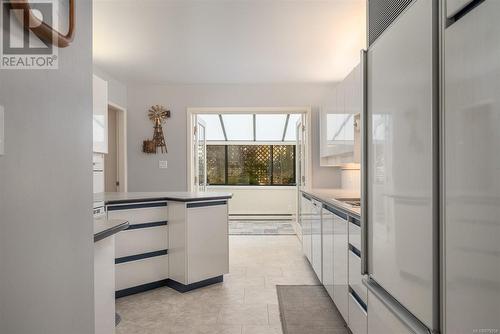 Kitchen with white cabinetry, baseboard heating, light tile patterned floors, and white refrigerator - 101 145 Newcastle Ave, Nanaimo, BC - Indoor Photo Showing Kitchen