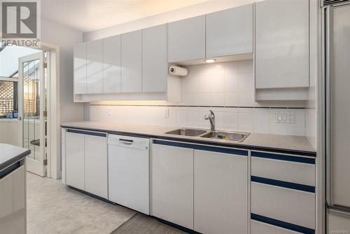 Kitchen with decorative backsplash, light tile patterned floors, white cabinetry, white dishwasher, and sink - 101 145 Newcastle Ave, Nanaimo, BC - Indoor Photo Showing Kitchen With Double Sink