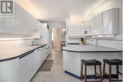 Kitchen with white cabinetry, sink, a kitchen bar, and white appliances - 