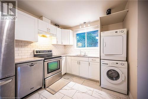 Kitchen with stainless steel appliances, white cabinets, decorative backsplash, sink, and stacked washer / dryer - 580 Highpoint Avenue Unit# Upper, Waterloo, ON - Indoor Photo Showing Laundry Room