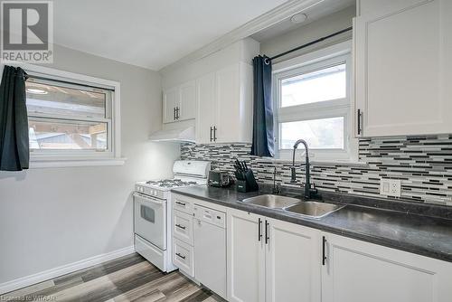 Kitchen featuring white cabinets, tasteful backsplash, wood-type flooring, sink, and white appliances - 824 Devonshire Avenue, Woodstock, ON - Indoor Photo Showing Kitchen With Double Sink