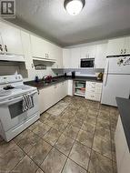 Kitchen with sink, ventilation hood, a textured ceiling, white appliances, and white cabinets - 