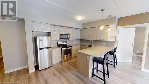 Kitchen featuring white cabinets, a breakfast bar area, pendant lighting, light wood-type flooring, and appliances with stainless steel finishes - 308 Lester Street Unit# 215, Waterloo, ON - Indoor Photo Showing Kitchen