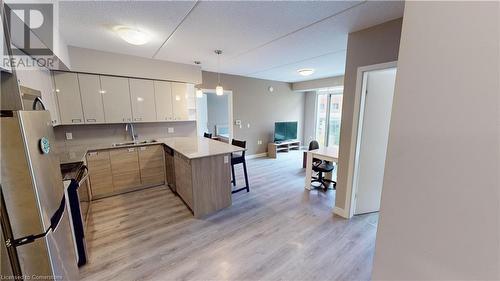 Kitchen with kitchen peninsula, white cabinetry, light wood-type flooring, appliances with stainless steel finishes, and decorative light fixtures - 308 Lester Street Unit# 215, Waterloo, ON - Indoor Photo Showing Kitchen With Double Sink