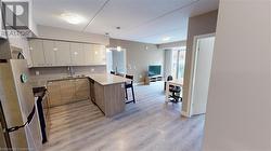 Kitchen with kitchen peninsula, white cabinetry, light wood-type flooring, appliances with stainless steel finishes, and decorative light fixtures - 