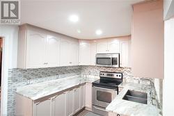 Kitchen featuring white cabinetry, appliances with stainless steel finishes, sink, and light stone counters - 