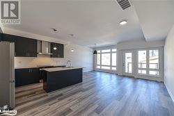 Kitchen featuring stainless steel appliances, wall chimney range hood, decorative light fixtures, dark hardwood / wood-style floors, and an island with sink - 