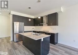 Kitchen with light wood-type flooring, appliances with stainless steel finishes, decorative light fixtures, sink, and wall chimney exhaust hood - 