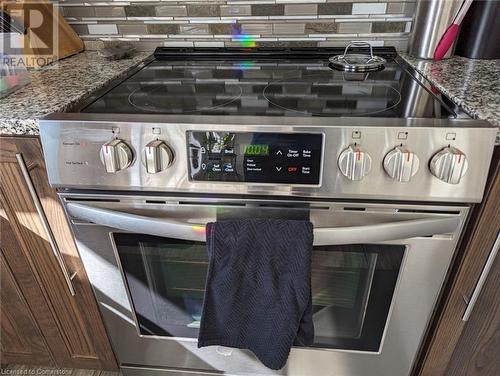 Interior details with decorative backsplash, dark brown cabinetry, stainless steel range with electric stovetop, and light stone countertops - 14 Greyhawk Street, Kitchener, ON - Indoor Photo Showing Kitchen