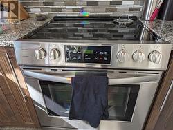 Interior details with decorative backsplash, dark brown cabinetry, stainless steel range with electric stovetop, and light stone countertops - 