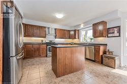 Kitchen with light tile patterned flooring, wall chimney exhaust hood, a kitchen island, and appliances with stainless steel finishes - 