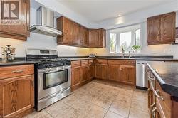 Kitchen featuring wall chimney range hood, sink, light tile patterned floors, and stainless steel appliances - 