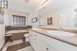 Bathroom with toilet, vanity, a relaxing tiled tub, and tile patterned flooring - 