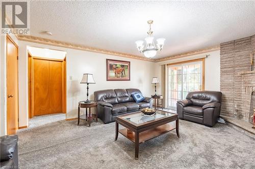 Living room featuring a fireplace, a textured ceiling, carpet flooring, and a notable chandelier - 46 Mark Place, Hamilton, ON 