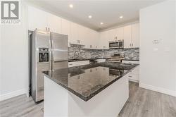 Kitchen with white cabinetry, stainless steel appliances, light hardwood / wood-style floors, and a center island - 