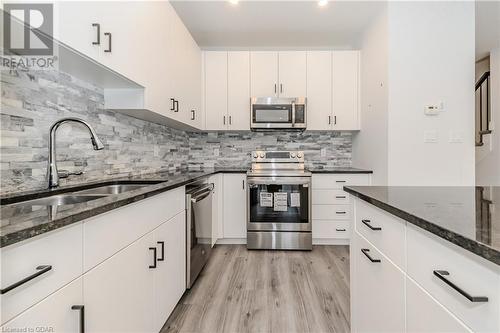 Kitchen featuring stainless steel appliances, sink, white cabinets, dark stone countertops, and light hardwood / wood-style flooring - 1023 Devonshire Avenue Unit# 3, Woodstock, ON - Indoor Photo Showing Kitchen With Double Sink With Upgraded Kitchen