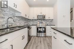 Kitchen featuring stainless steel appliances, sink, white cabinets, dark stone countertops, and light hardwood / wood-style flooring - 