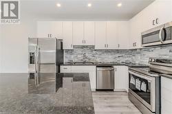 Kitchen with stainless steel appliances, white cabinets, sink, light hardwood / wood-style flooring, and dark stone countertops - 