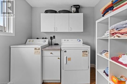 Clothes washing area featuring cabinets, washing machine and dryer, a textured ceiling, and dark wood-type flooring - 253 Auden Road, Guelph, ON - Indoor Photo Showing Laundry Room