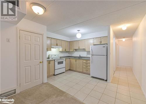 Kitchen with light tile patterned flooring, a textured ceiling, light brown cabinetry, sink, and white appliances - 107 Bond Street Unit# 201, Orillia, ON - Indoor Photo Showing Kitchen With Double Sink