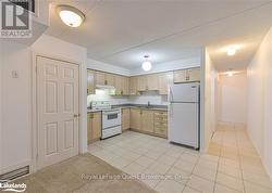 Kitchen with light tile patterned flooring, a textured ceiling, light brown cabinetry, sink, and white appliances - 