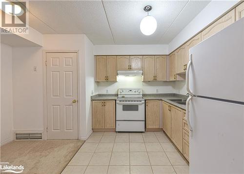 Kitchen featuring a textured ceiling, light tile patterned floors, light brown cabinetry, sink, and white appliances - 107 Bond Street Unit# 201, Orillia, ON - Indoor Photo Showing Kitchen With Double Sink