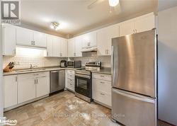 Kitchen with sink, appliances with stainless steel finishes, ceiling fan, backsplash, and white cabinets - 