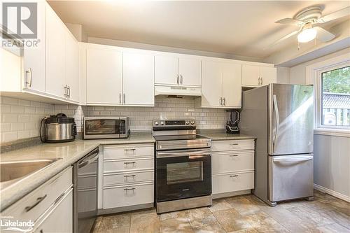 Kitchen with white cabinetry, light stone counters, appliances with stainless steel finishes, ceiling fan, and decorative backsplash - 441 Barrie Road Unit# 34, Orillia, ON - Indoor Photo Showing Kitchen