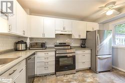 Kitchen with white cabinetry, light stone counters, appliances with stainless steel finishes, ceiling fan, and decorative backsplash - 