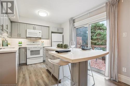 Kitchen featuring sink, tasteful backsplash, a kitchen breakfast bar, light wood-type flooring, and white appliances - 130 Livingston Avenue Unit# 21, Grimsby, ON - Indoor Photo Showing Kitchen