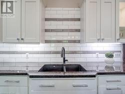 Kitchen featuring white cabinets, decorative backsplash, dark stone counters, and sink - 