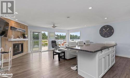 Kitchen featuring dark wood-type flooring, a kitchen island, a breakfast bar, crown molding, and white cabinetry - 64 Wolverine Beach Road, Port Severn, ON - Indoor With Fireplace