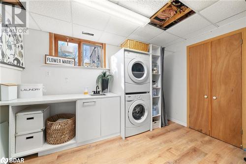 Laundry room featuring light wood-type flooring, cabinets, stacked washer / drying machine, and sink - 18133 Loyalist Parkway, Prince Edward County, ON - Indoor Photo Showing Laundry Room