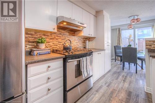 Kitchen with stainless steel appliances, a textured ceiling, decorative backsplash, light hardwood / wood-style floors, and white cabinets - 83 Bridlewreath Street, Kitchener, ON - Indoor Photo Showing Kitchen