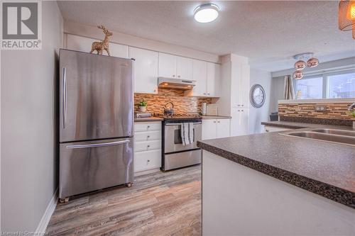 Kitchen with stainless steel appliances, light hardwood / wood-style floors, white cabinets, a textured ceiling, and sink - 83 Bridlewreath Street, Kitchener, ON - Indoor Photo Showing Kitchen With Double Sink