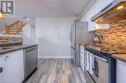 Kitchen with ventilation hood, backsplash, appliances with stainless steel finishes, hardwood / wood-style floors, and white cabinets - 