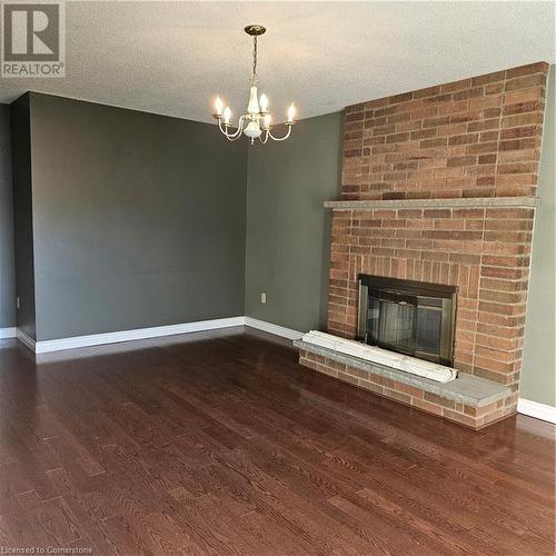 Unfurnished living room with a brick fireplace, a textured ceiling, dark hardwood / wood-style flooring, and a notable chandelier - 115 Cranston Avenue, Cambridge, ON - Indoor Photo Showing Living Room With Fireplace