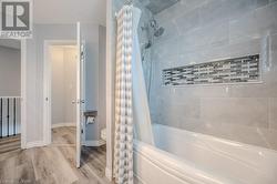 Bathroom featuring wood-type flooring, toilet, and shower / bath combination with curtain - 