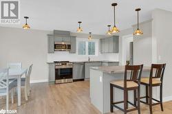 Kitchen with gray cabinetry, hanging light fixtures, light hardwood / wood-style floors, and stainless steel appliances - 