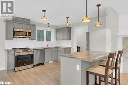 Kitchen with stainless steel appliances, backsplash, decorative light fixtures, gray cabinets, and light hardwood / wood-style floors - 