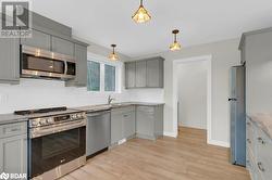 Kitchen featuring gray cabinetry, light wood-type flooring, appliances with stainless steel finishes, backsplash, and pendant lighting - 