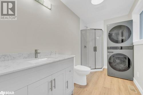 Bathroom featuring toilet, hardwood / wood-style flooring, vanity, walk in shower, and stacked washer / drying machine - 530 Addington Road 5, Cloyne, ON - Indoor Photo Showing Laundry Room